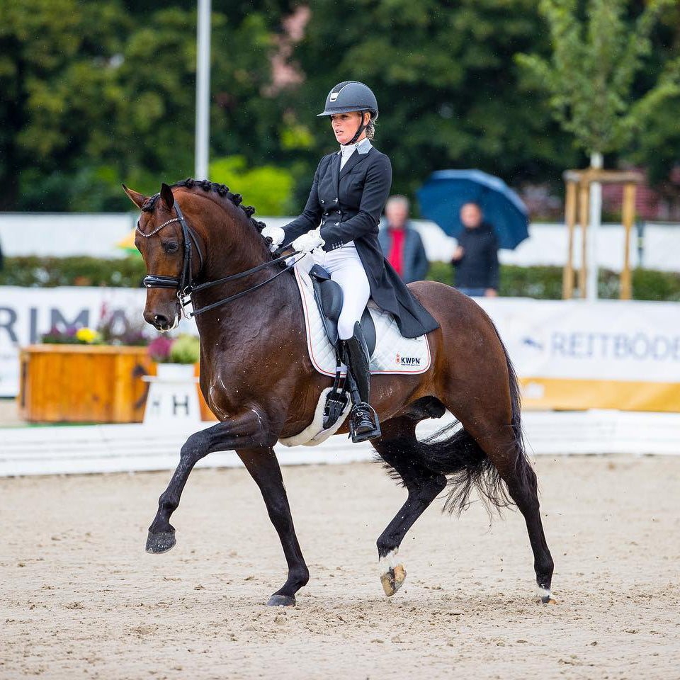 Model riding extended trot while wearing JuulC' Black Light Grey Women's Dressage Frack made from sport-tech merino wool 